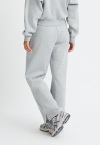 Pantalones deportivos grises de tejido suave, con un ajuste relajado y piernas rectas, combinados con zapatillas deportivas con detalles de malla y patrones.