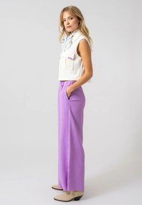 Witte cropped top met voorkanten, gecombineerd met lichtpaarse, geribbelde broek met hoge taille. Beige hakken maken de outfit af.