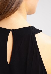 Top negro sin mangas con un diseño de ojal en la parte posterior y un pequeño cierre de botón. Fabricado en una tela suave con una textura lisa.