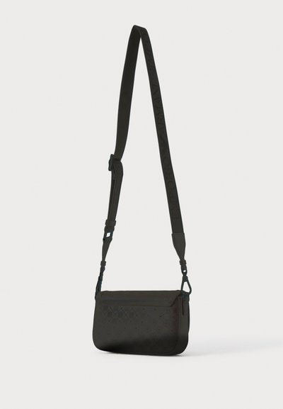 Μαύρη τσάντα χιαστί με ρυθμιζόμενο λουρί, σκαλισμένο το όνομα της μάρκας και μικρό διάτρητο διαμάντι μοτίβο στην μπροστινή πτέρυγα.