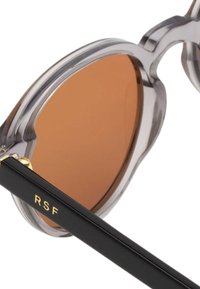 Occhiali da sole rotondi con montatura in acetato trasparente, lenti marroni e aste nere con dettagli in oro e le lettere "RSF".