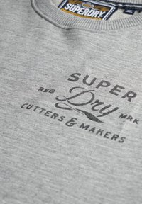 Szary sweatshirt z prążkowanym dekoltem, miękką teksturą oraz czarnym nadrukiem z tekstami "SUPER DRY" i "CUTTERS & MAKERS".