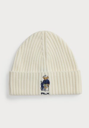 Kremfarget ribbet lue med en farget brodert bjørn som har på seg en blå frakk. Logoen "RLX" er brodert på bunnen av kanten.