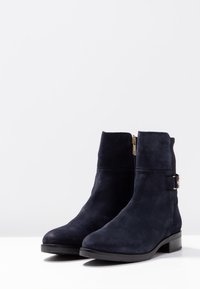 Námořnické semišové kotníkové boty s texturovaným povrchem, bočním zipem a zlatým sponou. Nízký zúžený podpatek zajišťuje stabilitu.