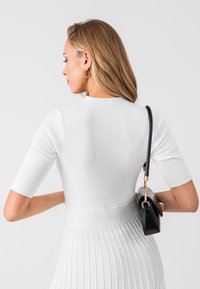 Haut blanc à rayures avec des manches courtes, design ajusté et finition texturée ; associé à un petit sac à main noir.