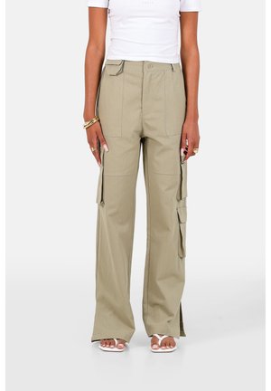 Frau trägt beige weite Cargohosen, weißes bauchfreies Top, weiße Sandalen sowie goldene Ringe und Armbänder an den Händen.