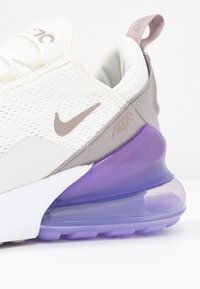 Zapatilla Nike Air Max 270 en malla blanca y gris claro con una suela de amortiguación de aire morada. Presenta una pestaña de agarre y detalles sutiles de la marca.