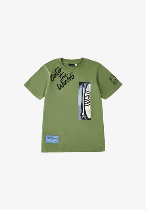 Maglietta verde a maniche corte con la scritta "Catch the Waves", grafica di una tavola da surf sul davanti e una toppa blu "Gold Coast" vicino all'orlo.
