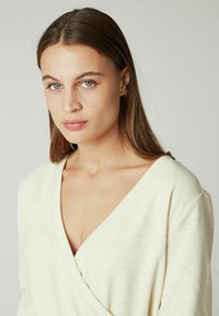 Haut crème à col en V, à manches longues, avec une texture douce et une coupe décontractée. Design enveloppant remarquable et léger élasticité dans le tissu.