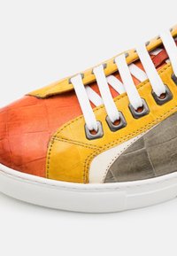 Baskets avec des lacets blancs et des panneaux en cuir multicolores en orange, jaune, gris et blanc, gros plan sur le côté et la zone des orteils.