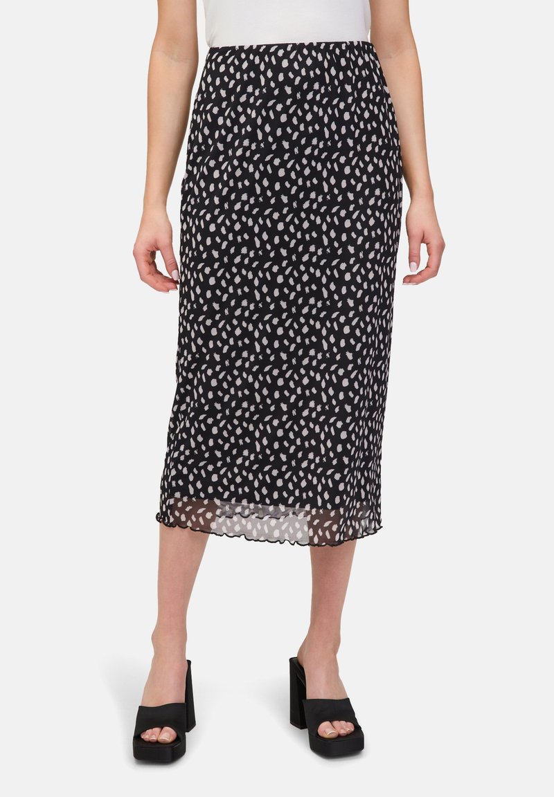 Jupe midi noire avec un motif blanc en forme de feuilles, fabriquée en tissu léger. Ourlet festonné, portée avec des sandales plates-formes noires épaisses.