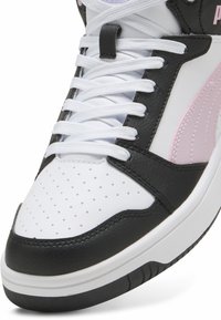 White and black high-top sneaker made of leather, featuring pink accents, perforated toe box, and flat white laces. Round rubber sole.
