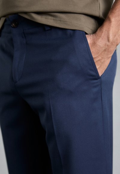 Námornícke modré nohavice s hladkou textúrou, so bočnými vreckami a gombíkovým zapínaním, skombinované s olivovo zeleným topom.