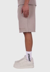 Beige bomulds shorts med en afslappet pasform, med et broderet logo på kanten. Båret med hvide sokker og beige sneakers.