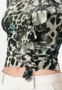 Top cu imprimeu de leopard, dintr-un material ușor, cu accente negre și teal, detalii cu volane de-a lungul gâtului și o siluetă ajustată.