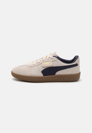 Baskets basses en daim beige Puma avec semelle gomme, bande latérale noire, lacets crème et logo doré « Puma Palermo » sur le côté.