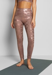Leggings de camuflaje en color oro rosa, confeccionados en una tela suave y elástica, con una cintura alta y corte hasta el tobillo, combinados con un top corto a juego.