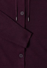 Cárdigan de punto burdeos con cierre de botones, puños acanalados y detalle de cordón en la capucha. Textura suave y diseño casual.