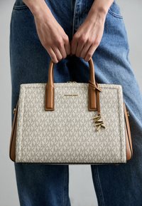 Borsa strutturata in beige chiaro con motivo a logo, manici e dettagli in pelle marrone. Presenta un dettaglio a forma di charm dorato.