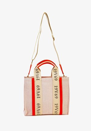 Sac fourre-tout en toile rose clair avec des accents rouges. Dispose de deux larges anses beiges avec le texte "1969". Forme structurée avec une fermeture éclair.
