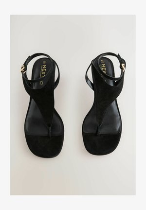 Sandale negre din suedă cu un design cu bareta pentru degetul mare, curea ajustabilă pentru gleznă și talpă plată, netedă. Accente din metal auriu pe curea.