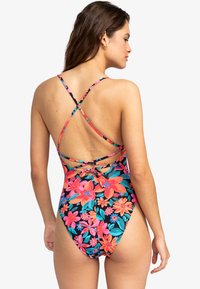 Maillot de bain une pièce fleuri avec des bretelles croisées, couleurs vives de rose, orange et bleu sur un fond noir, offrant un dos ouvert.