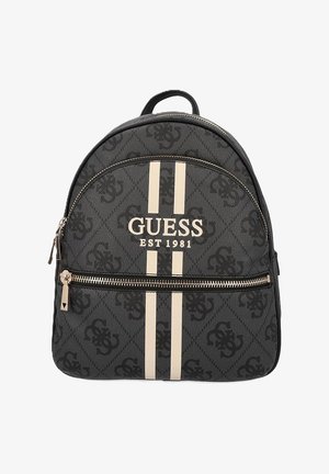 Sac à dos en toile noir avec des rayures beiges, logo "GUESS EST 1981", motif texturé, et poche frontale zippée avec quincaillerie métallique.
