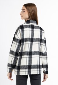 Camicia in pile con un motivo a quadri bianco e nero, caratterizzata da un colletto alto, bottoni sulle maniche e una vestibilità comoda.