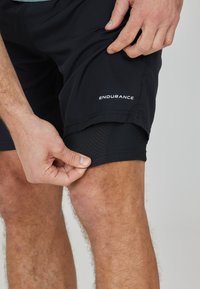 Schwarze Sportshorts aus leichtem Material. Netzfutter am Saum sichtbar. Mit dem weißen "ENDURANCE"-Logo an der Seite.