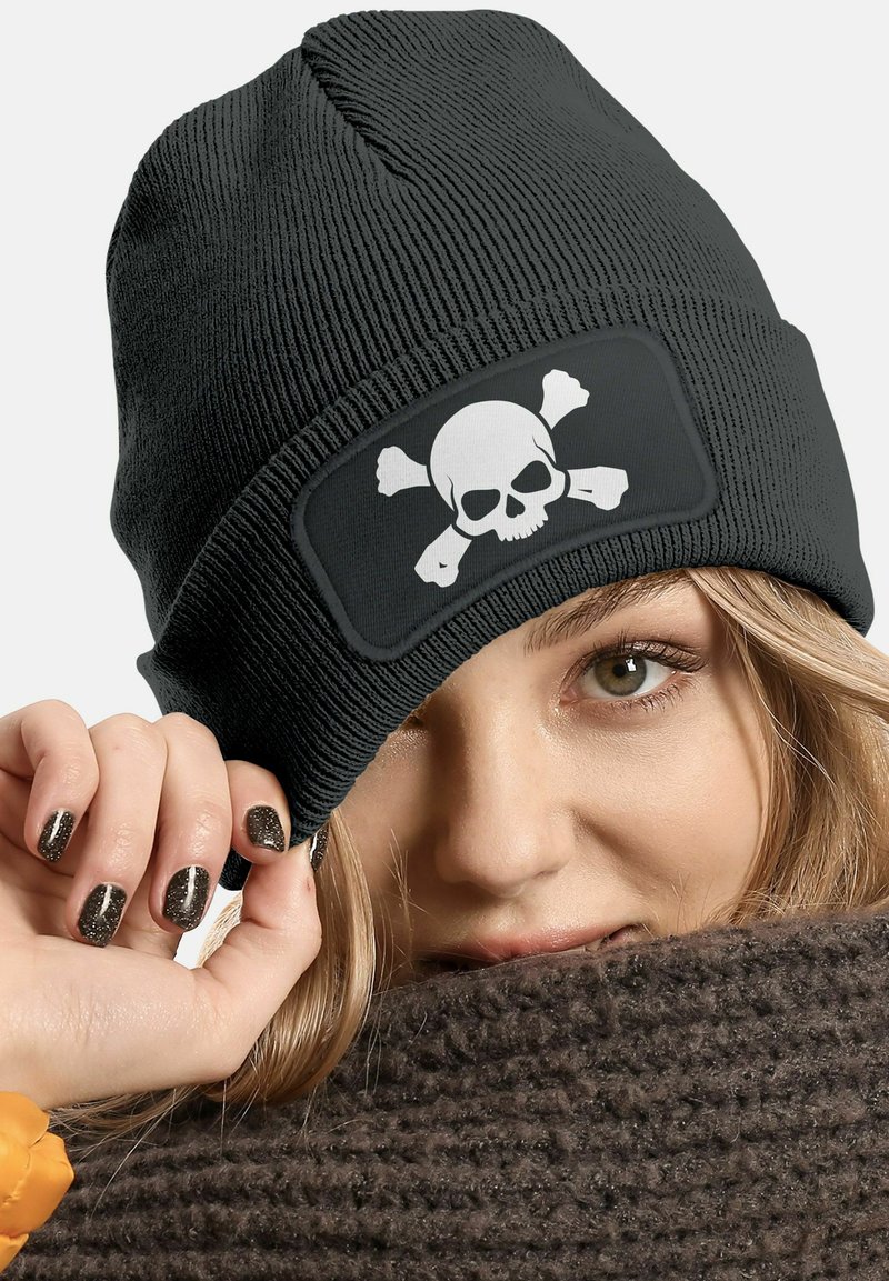 Schwarze Beanie-Mütze mit gerippter Textur, die ein weißes Totenkopf- und Kreuzbeinig-Design auf einem rechteckigen Patch zeigt.