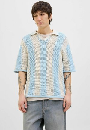 Strikket polo med korte ærmer i lyseblå og creme striber, der har V-hals og en afslappet pasform. Bærer en hvid undertrøje med synlige tatoveringer.