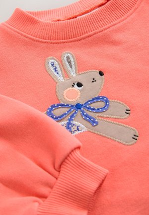 Koraalrode trui met een geribde halslijn, met een geborduurd konijnendesign met een blauw gestippelde strik en beige details.