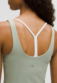 Jasnozielony top sportowy z głębokim dekoltem z tyłu, białe kontrastowe ramiona tworzące design typu racerback, gładka tekstura i logo marki z tyłu.