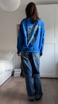 Sweat-shirt bleu avec un motif floral dans le dos ; associé à un jean bleu délavé et ample. Design simple, texture de tissu décontractée.