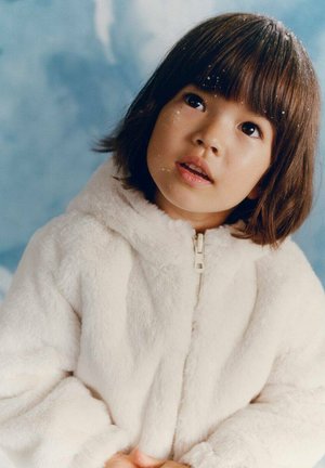 White, fluffy zip-up jacket with a hood, featuring a soft texture. Child with short, dark hair gazing upward against a soft blue background.