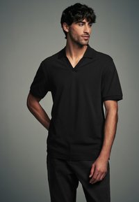 Polo shirt nero a maniche corte con design a scollo a V. Realizzato in tessuto liscio, presenta una vestibilità classica e una texture sottile. Nessun motivo visibile.