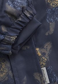 Marinfärgad tyg med ett houndstooth-mönster och gula hundillustrationer. Samlade manschetter med en jämn textur och en etikett märkt "minymo."