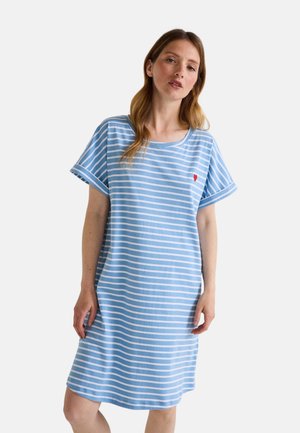 Femme portant une robe à rayures horizontales bleu clair et blanches avec des manches courtes et un petit cœur rouge sur le côté gauche de la poitrine, debout devant un fond blanc.