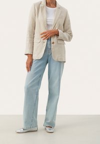 Beige liina bleiseri, jossa on halkio kaulus ja etunappi, yhdistettynä vaaleansiniisiin suoriin farkkuihin ja hopeisiin teräväkärkisiin kenkiin.