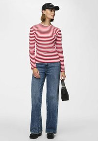 Röd och vitrandig långärmad skjorta som matchas med högmidjade blå jeans, svart keps och en liten svart handväska. Tjockt, mjukt tyg.