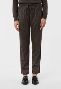 Person wearing brown drawstring pants and black loafers, standing against a white background.