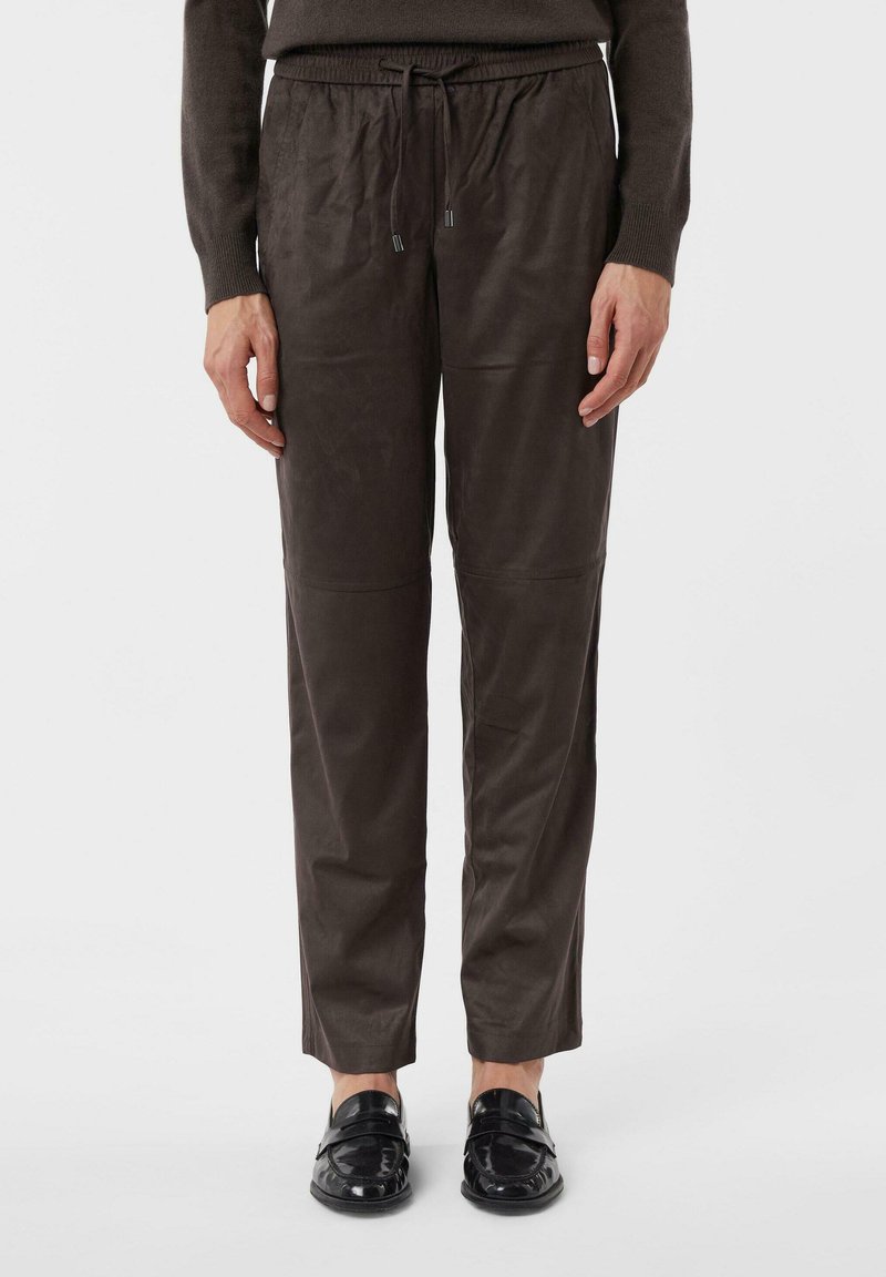 Person wearing brown drawstring pants and black loafers, standing against a white background.