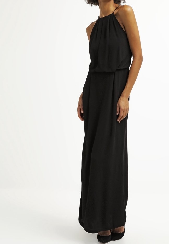Femme portant une robe maxi noire sans manches avec un col halter, un haut plissé ample et une taille cintrée, debout devant un fond blanc uni.