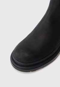 Sort læder ankelstøvle med rund tå og tekstureret gummisål. Overdelen er glat og har et enkelt design med minimale detaljer.