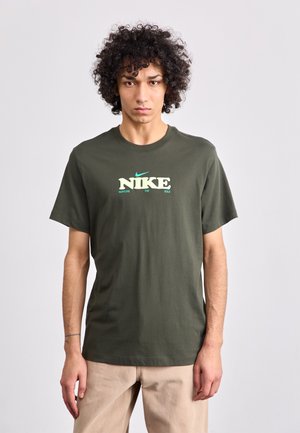 Oliven grøn bomulds t-shirt med korte ærmer, med "NIKE" logo i hvid og lys grøn tekst. Klassisk rund halsudskæring og afslappet pasform.
