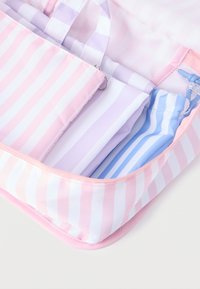 Τρεις υφασμάτινες θήκες με ρίγες σε ροζ, λεβαντό και μπλε μέσα σε μια ροζ και λευκή ριγέ τσάντα με φερμουάρ.