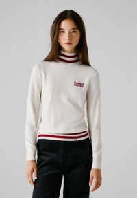 Maglione bianco a maniche lunghe con colletto alto, dettagli a righe rosse e bianche, feature "Red Bull RACING" ricamato in rosso sul petto.