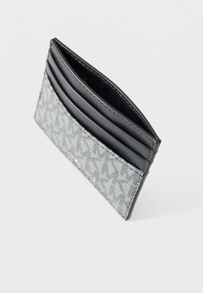 Porte-cartes gris mince avec devant en tissu à motifs et plusieurs emplacements pour cartes en cuir noir, incliné sur fond blanc.