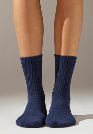 Calze a coste blu navy realizzate in materiale morbido, caratterizzate da una lunghezza a metà polpaccio e una calzata aderente attorno alla caviglia. Nessun motivo o accento visibile.