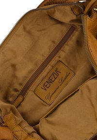 Braune Echtledertasche mit Innenfutter in Beige und einem Reißverschlussfach. Mit einem Etikett mit der Aufschrift "VENEZIA Genuine Leather." Glatte Textur.